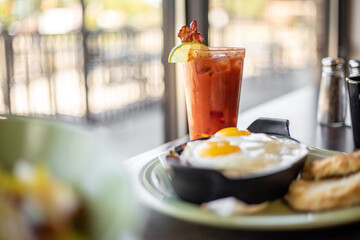 A bloody mary beverage cocktail with two eggs near a bright window at a modern brunch diner café