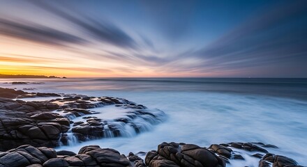 Serene coastal sunset with long exposure waves crashing over rugged rocks