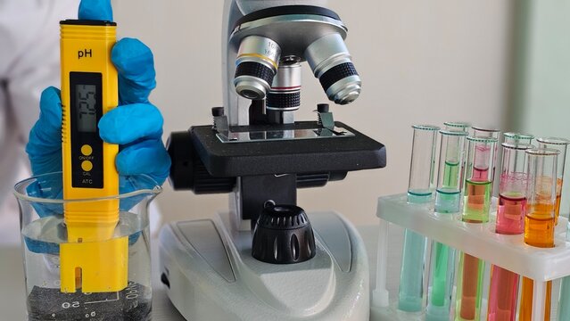 Testing water acidity with a pH meter beside a microscope and colorful test tubes