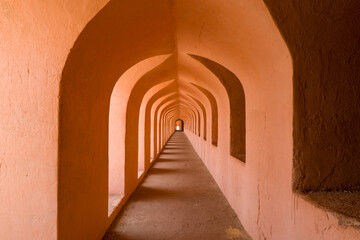 Long corridor with repeating pointed arches and textured terracotta walls at Imambara Bara in Lucknow. Warm sunlight casts soft shadows, emphasizing depth and architectural rhythm in the historic