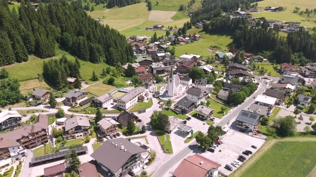 Fly over the Filzmoos Dachstein valley during summer across a village and juice green grass fields