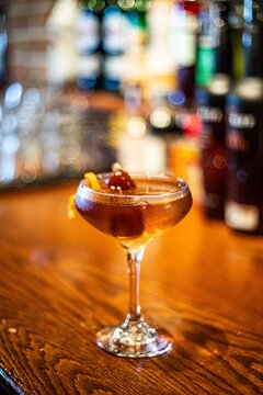 A manhattan in a coupe glass served on a wooden restaurant bar during happy hour at a restaurant