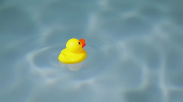 A bright yellow rubber duck with red beak floats peacefully on rippling blue water