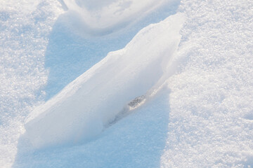 Jagged ice shard resting in sparkling white snow with blue shadows on a sunny day