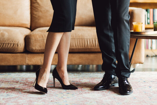 Close-up of a man and woman's legs in formal shoes standing on a carpet.