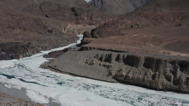 Drone reveal glides to showcase frozen Zanskar River with ice-turquoise patches nestled between sheer rocky canyon walls in Ladakh India.
