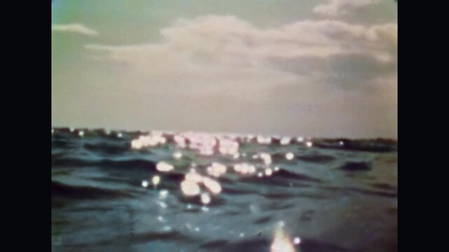 Close up, shiny sea waves sparkling in bright summer sun light. Abstract blue ocean surface with water ripples, reflections under blue sky background. Old film. Archival retro 1970s. Vintage archive