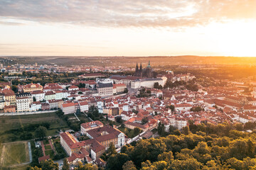Fototapeta premium At sunrise, Prague Castle stands majestic against the golden light, casting a warm glow over the city. The rooftops and lush greenery create a stunning panorama of Prague rich history.