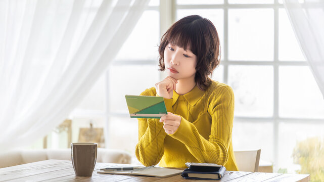 銀行の預金通帳を確認する女性, Woman checking a bank passbook at home