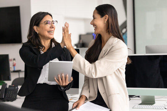 Mature 60s and young 30s women teammates exchanging friendly high five gesture, symbolizing successful intergenerational teamwork outcome and mutual respect. Collaboration, support and team spirit