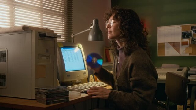 Medium side shot of cheerful young Caucasian woman inserting cd-rom disk with software program into drive, while working on business report on vintage computer in cozy cluttered home office