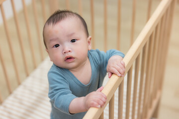 Adorable infant holding rail and standing inside baby crib