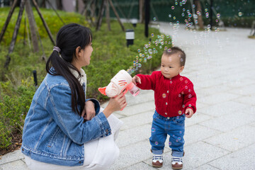 Mum and baby son playing with bubble machine outdoor
