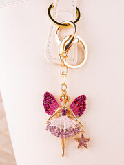 Close-up of a bright metal keychain in the shape of a fairy with wings made of pink rhinestones on a white bag