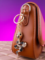 Close-up of a bright metal keychain in the shape of a black snake made with rhinestones on a brown  bag