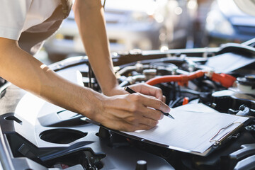 Naklejka premium Auto check, car service shop concept. Automobile repairman writing job checklist on clipboard, mechanic checking engine to estimate repair machine, inspecting maintenance by engineer at vehicle garage