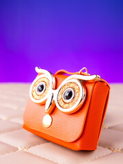 A close-up of a small orange leather mini bag featuring an owl design with bright, expressive eyes