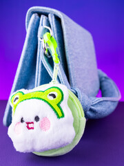 A close-up of a soft, green plush wallet featuring a fun white monster design on blue bag