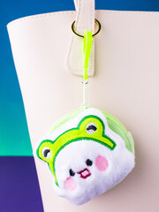 A close-up of a soft, green plush wallet featuring a fun white monster design on blue bag