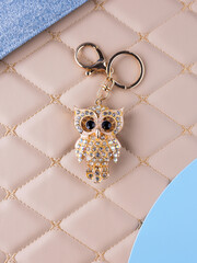 A close-up of a metal keychain in the shape of an owl adorned with white rhinestones, placed on a leather surface.