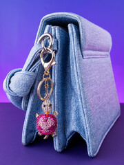 A close-up of a metal keychain in the shape of a turtle decorated with pink rhinestones, placed  on  blue bag