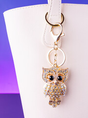 A close-up of a metal keychain in the shape of an owl adorned with white  rhinestones on  white bag