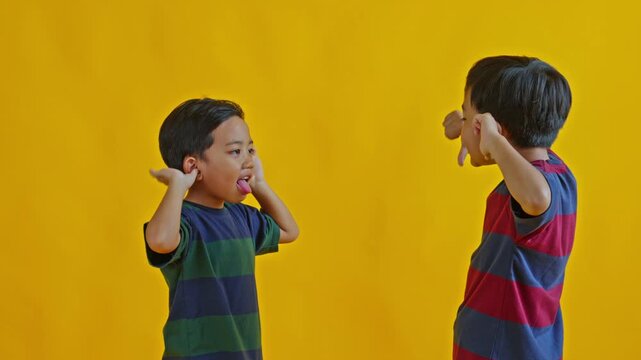 Playful little siblings making funny faces and sticking their tongues out isolated on yellow background