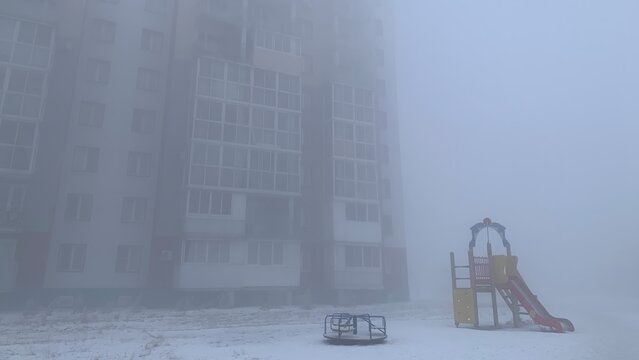 Foggy Winter Apartment Building and Empty Playground in Snow
