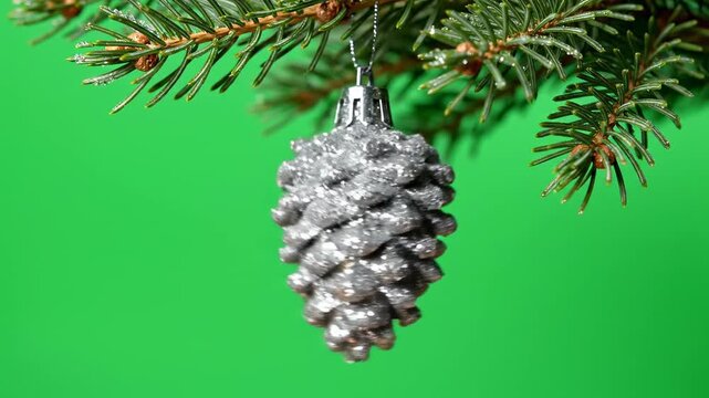 Isolated macro close-up of a silver glitter-coated pinecone ornament swinging gently on a green Christmas tree branch against a pure chroma key green screen alpha channel, branch, swinging gently