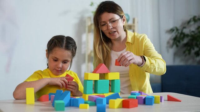 Playing with colorful blocks together mother and child build toy tower on table while parent guides toddler in playful learning activity preschool age family block stacking and cooperative play
