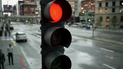 Bright red traffic light stands tall in a bustling city street. Raindrops glisten on the pavement as pedestrians cross safely, showcasing a vibrant urban life at twilight. © icetray