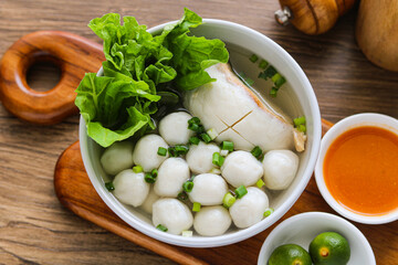 A delicious bowl of Bakso Ikan and Bakso Tahu Ikan, featuring white fish balls and savory stuffed tofu in a light, clear broth. Garnished with lettuce and chopped spring onions.