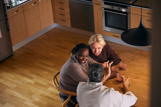 High angle view of childhood friends enjoying drinks with each other while sitting at table in home