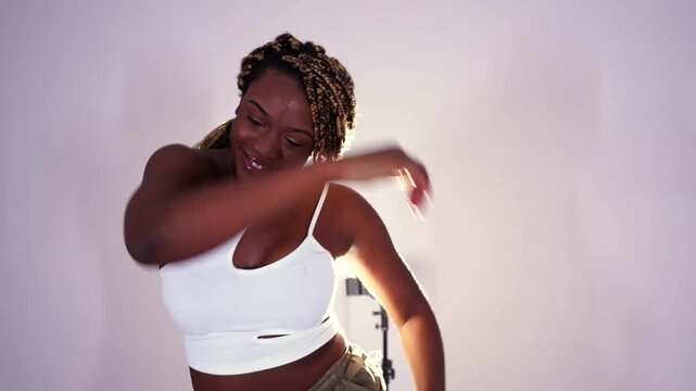 Beautiful young black woman with long braids energetically dancing afrodance. A professional dancer performing modern choreography in a studio