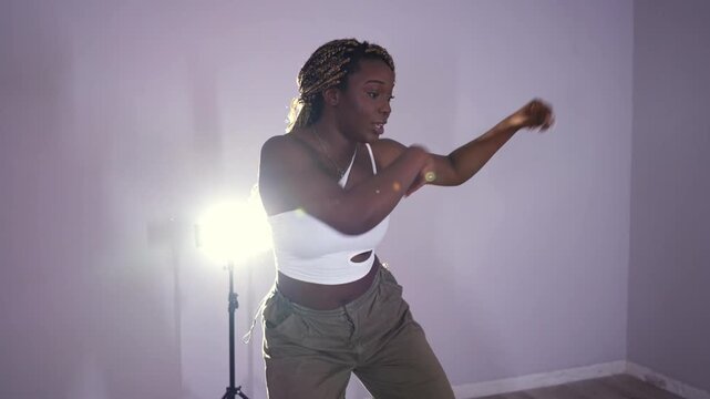 Young energetic african american woman with braids dancing afrodance in a studio. Beautiful female performer rehearsing a modern choreography