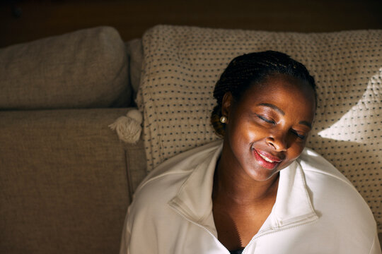 High angle view of smiling mature woman leaning on sofa with eyes closed in home