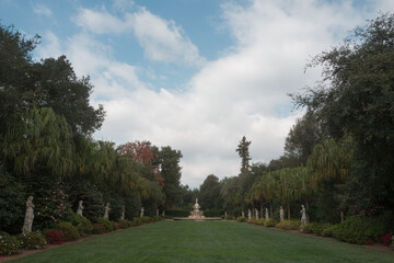 Obraz premium Formal garden pathway with statues, fountain, and manicured green lawn