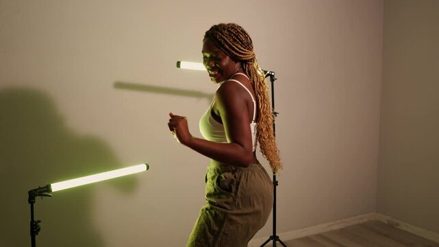 Passionate african woman with braids dancing contemporary afrobeats in a modern studio. Energetic female performer moving to the music