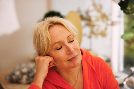 Relaxed blond senior woman leaning on elbow with eyes closed