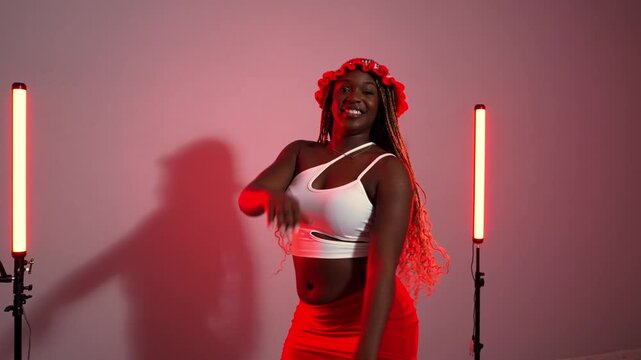 Beautiful young black woman with long braids energetically dancing afrodance. Stylish female performer moving to the rhythm in a studio