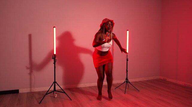 Energetic african woman with braids dancing to afrobeats music. Joyful female dancer performing modern choreography in a studio with red lights