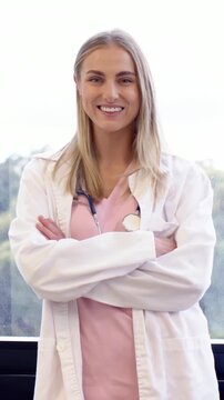Vertical video: Posing woman Dr arms crossed in white coat steth to camera smiling in clinic