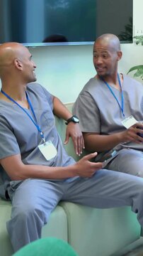 Vertical video: Tapping phone, man leaning in on staff couch in gray scrubs and IDs, sharing clip