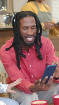 Vertical video: Pulling phone, dreadlocked red-shirted man sharing photos at cafe, copy space