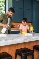 Indian father and son cleaning marble countertop in kitchen using spray bottles and cloth © wavebreak3