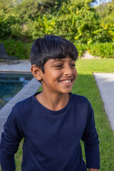 Asian child boy standing on lawn in backyard near pool and smiling by patio edging