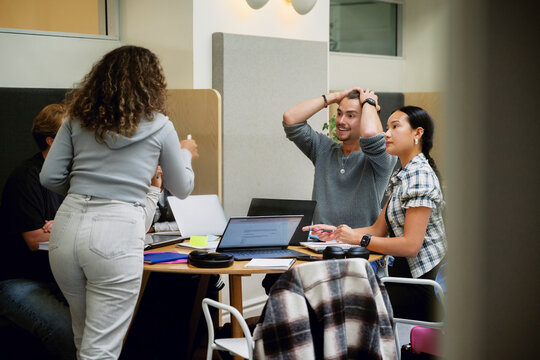 Young man with hand in hair sitting for group discussion at university campus