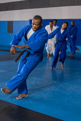 Diverse dojo students in gis belts following african american instructor stepping on mats