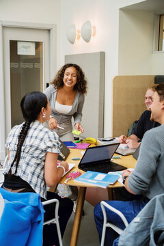 Smiling young woman enjoying with friends during group study in college campus