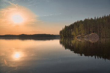 Obraz premium A tranquil lake at sunset with a reflective water surface, silhouetted shores and a warm evening sky, creating a peaceful and meditative atmosphere.